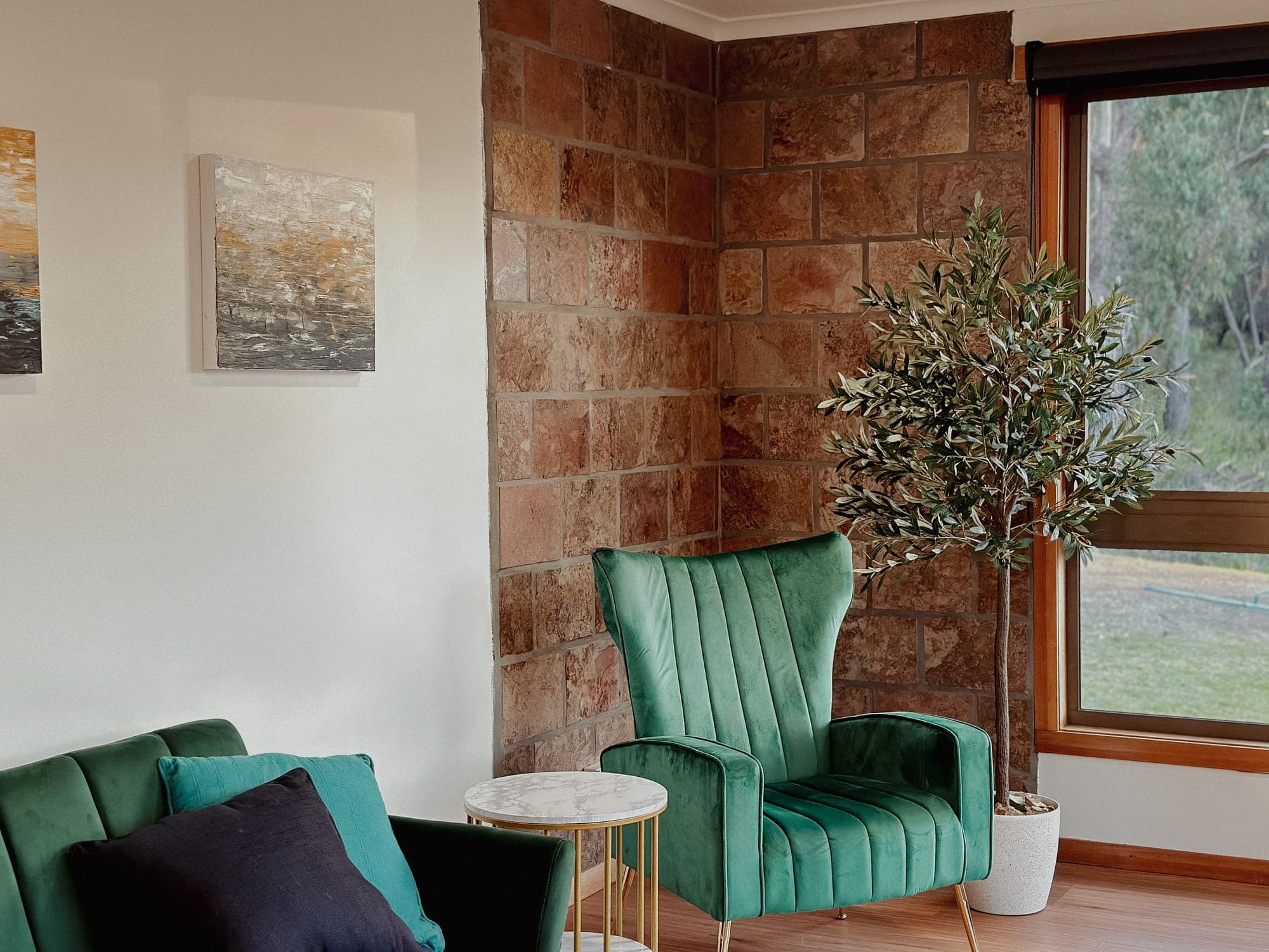 LunaStay — emerald wingback armchairs against the brick feature wall